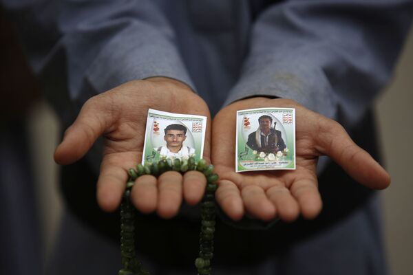 أحد المواطنين يحمل على راحتيه صور أقربائه القتلى - سبوتنيك عربي
