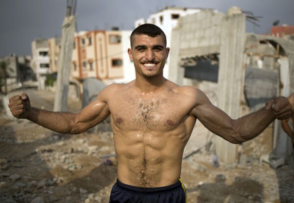 فلسطيني يعرض عضلاته على خلفية الأنقاض في مدينة غزة - سبوتنيك عربي