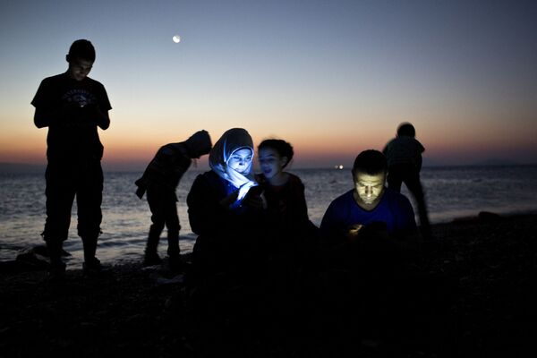 مهاجرين يتفقدون هواتفهم على اليابسة في جزيرة كوس اليونانية بعد رحلة طويلة في قوارب مطاطية - سبوتنيك عربي