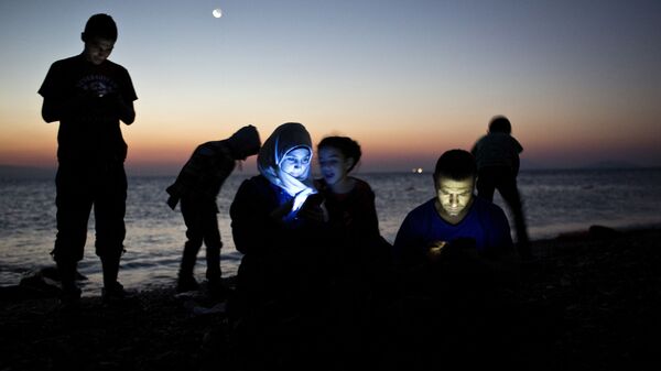 مهاجرين يتفقدون هواتفهم على اليابسة في جزيرة كوس اليونانية بعد رحلة طويلة في قوارب مطاطية - سبوتنيك عربي