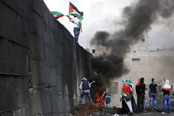 المتاظهرون الفلسطينيون يحاول تدمير الجدار الفاصل بين أبو ديس والقدس الشرقية،  خلال الاشتباكات بين الفلسطينيين وقوات الإحتلال الإسرائيلي في الضفة الغربية، 28 أكتوبر/ تشرين الأول 2015. - سبوتنيك عربي