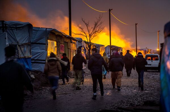 مهاجرون يركضون باتجاه مكان الحريق المشتعل في مخيم للمهاجرين اسمه Jungle (الغابة) في كالي بفرنسا، 1 مارس/ آذار 2016. - سبوتنيك عربي