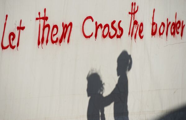 ظل طفلين لاجئين ينعكس على حائط بالقرب من قرية إيدوميني اليونانية، مكتوب عليها فلنعبر هذا الحاجز!، 4 مايو/ آيار 2016. - سبوتنيك عربي