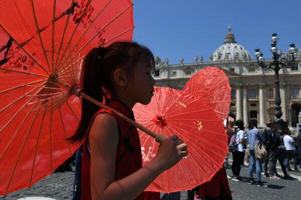 طفلة تحمل مظلة حمراء وتسير من أمام مقر البابا في الفاتيكان، 22 مايو/ آيار 2016. - سبوتنيك عربي