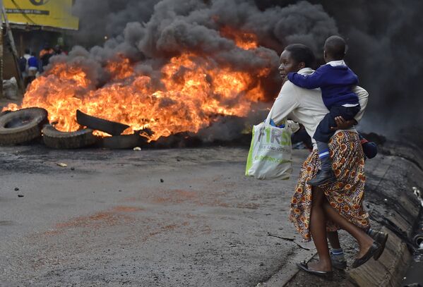 امرأة تحمل طفلها وتمر بالقرب من عجلات تحترق في شوارع نيروبي بكينيا، 23 مايو/ آيار 2016. - سبوتنيك عربي