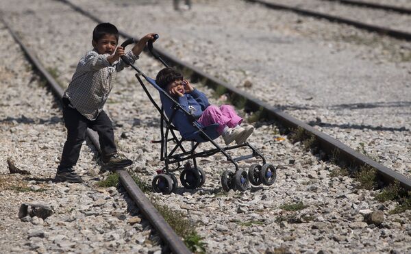 Мальчик везет коляску с ребенком в лагере беженцطفلين لاجئين، أحدهما يدفع بالآخر في قرية إيدوميني باليونان، 22 مايو/ آيار 2016.ев в Идомени, Греция - سبوتنيك عربي