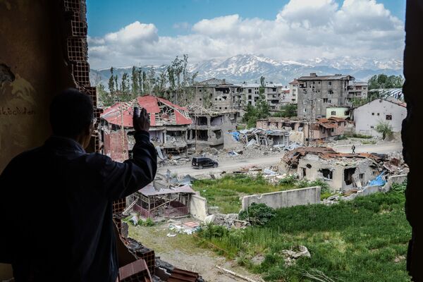 رجل يقف على خلفية ركام المباني في المنطقة التي تعرضت للاشتباكات بين القوات التركية والكردية في مدينة يوكسيكوفا بالقرب من الحدود مع العراق وإيران، 30 مايو/ أيار 2016. - سبوتنيك عربي