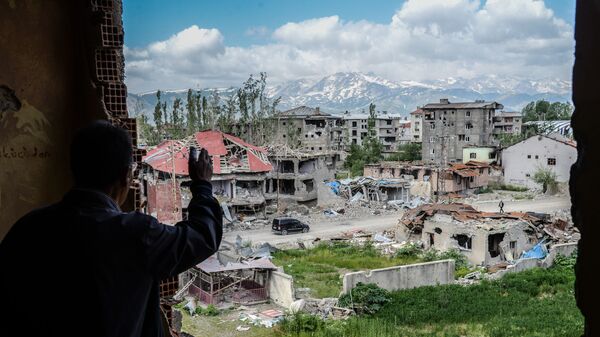 رجل يقف على خلفية ركام المباني في المنطقة التي تعرضت للاشتباكات بين القوات التركية والكردية في مدينة يوكسيكوفا بالقرب من الحدود مع العراق وإيران، 30 مايو/ آيار 2016. - سبوتنيك عربي
