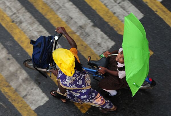 فتاة هندية تحمل شمسية وهي راكبة دراجة هوائية تقطع الطريق في تشيناي، 8 يونيو/ حزيران 2016. - سبوتنيك عربي