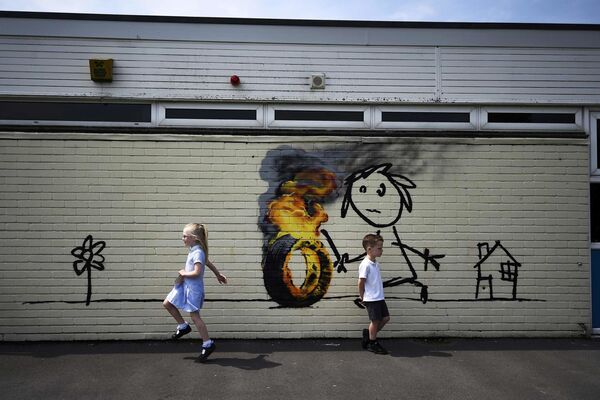أطفال يلعبون على خلفية جدارية للفنان بانكسي (Banksy) على جدار لمدرسة الابتدائية في بريستول، بريطانيا 6 يونيو/ حزيران 2016. - سبوتنيك عربي
