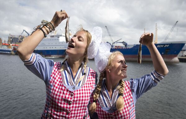 فتاتان ترتديان زياً تقليدياً هولندياً وتتصوران مع سمك الفسيخ نيو هارينغ في ميناء سخيفينينغن، 14 يونيو/ حزيران 2016. وذلك من أجل مزاد خيري بقيمة 90000. - سبوتنيك عربي