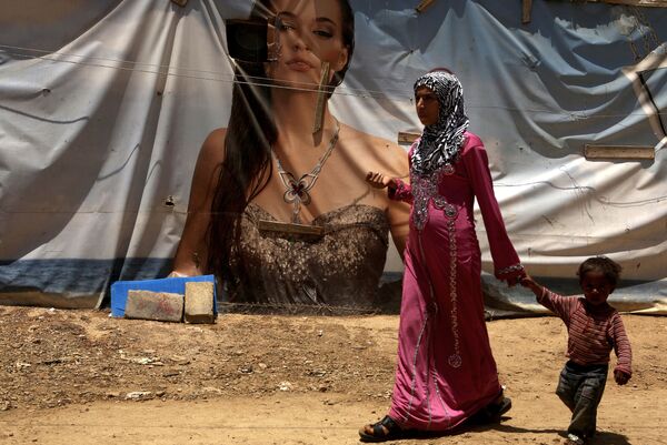 لاجئة سورية من حلب وطفلها على خلفية خيمة عليها رسم إعلاني، مخيم اللاجئين في لبنان 20 يونيو/ حزيران 2016 - سبوتنيك عربي