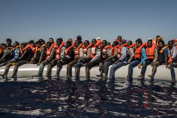 لاجئون من إرتيريا ومالي وبنغلادش (ودول أخرى) ينتظرون قارب نجاة في البحر الأبيض المتوسط على بعد 27 كم عن شواطئ ليبيا، يوليو/ تموز 2016 - سبوتنيك عربي