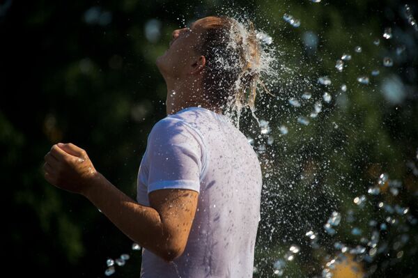 رجل يهرب من حر الجو إلى نافورة المياه زافيسا على ساحة مانيجنايا في موسكو - سبوتنيك عربي