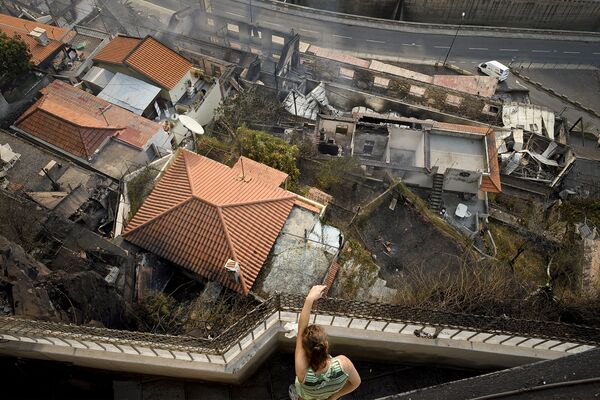 امرأة تقف على شرفة منزلها المطل على آثار حريق لمنزل مجاور في كامبو دا بارسا، جزيرة ماديرا، 10 أغسطس/ آب 2016 - سبوتنيك عربي