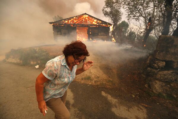 امرأة تهرب من الحريق في قرية أوتيرو، خلال اندلاع الحرائق الهائلة التي تشهدها البرتغال في الآونة الأخيرة، 13 أغسطس/ آب 2016 - سبوتنيك عربي