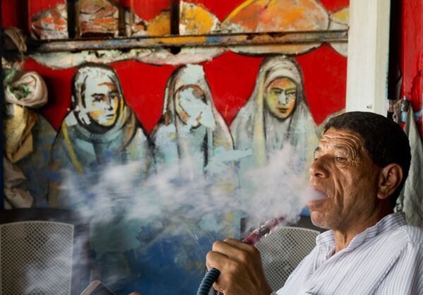 رجل يدخن ووراءه معرض اللوحات الفنية - سبوتنيك عربي