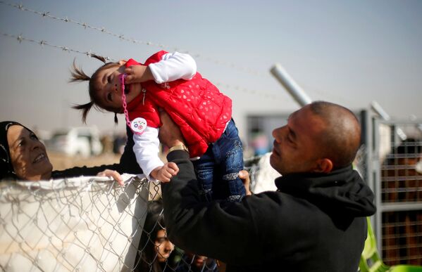 نازح عراقي من الموصل، يمرر ابنته لترى جدتها من خلال عازل بمخيم للنازحين، العراق 28 نوفمبر/ تشرين الثاني 2016 - سبوتنيك عربي