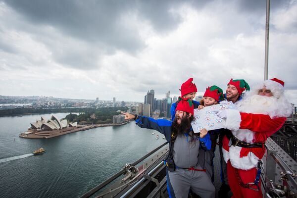 مجموعة من أشخاص يرتدون زس سانتا كلاوز يقفون أعلى جسر سيدني هاربر بريدج ويشيرون إلى المنازل التي سيرسلون الهدايا إليها، أستراليا، 7 ديسمبر/ كانون الأول 2016 - سبوتنيك عربي