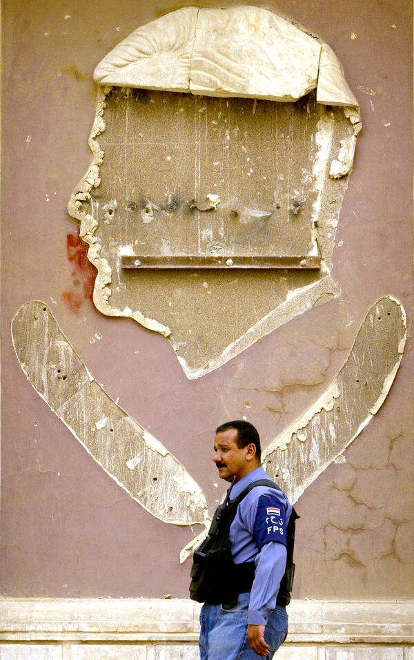 شرطي عراقي على خلفية جدار كانت عليه صورة للرئيس العراقي السابق صدام حسين، 20 أكتوبر/ تشرين الأول 2005 - سبوتنيك عربي
