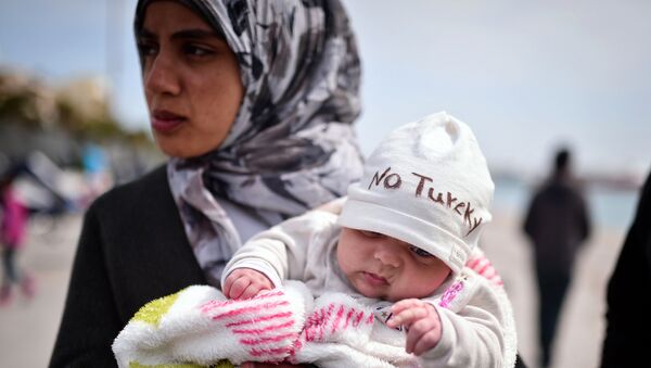 A Syrian refugee holds a two-month old baby as refugees and migrants who broke out from Chios detention camp, and camped out in the port of the city, stage a protest with their children chanting 'No Turkey' on April 3, 2016. - سبوتنيك عربي