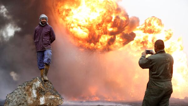 رجل يلتقط صورة لصديقه، بينما يقف الأخير على خلفية نيران مشتعلة ودخان كثيف، نتيجة اندلاع الحرائق في آبار نفط في القيارة، العراق، 30 يناير/ كانون الثاني 2017 - سبوتنيك عربي