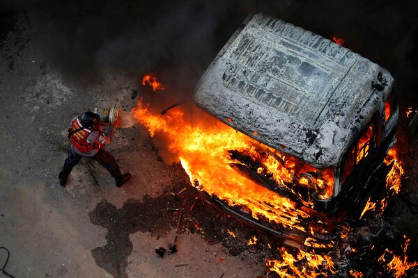 إطفاء حريق اندلع في سيارة خلال احتجاجات عارمة ضد حكومة الرئيس نيكولاس مودورو في كاراكاس، فنزويلا 24 أبريل/ نيسان 2017 - سبوتنيك عربي