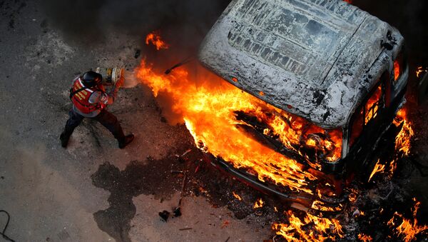 إطفاء حريق اندلع في سيارة خلال احتجاجات عارمة ضد حكومة الرئيس نيكولاس مودورو في كاراكاس، فنزويلا 24 أبريل/ نيسان 2017 - سبوتنيك عربي
