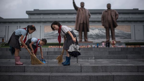 تلاميذ ينظفون الدرج الذي يقود إلى تماثيلي الزعيمين الكوريين الشماليين الراحلين كيم إيل سونغ وكيم جونغ إيل، على تلة مانسو حيث تصادف البلاد يوم النصر فى بيونغ يانغ، كوريا الشمالية فى 27 يوليو/ تموز 2017 - سبوتنيك عربي