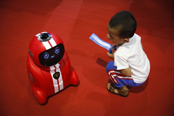 طفل يحمل تذكرة دخول ينظر إلى رجل آلي (يتميز بالتعلم الذاتي) خلال المؤتمر الدولي للرجال الآليين في ييتشوانغ في بكين،  23 أغسطس/ آب 2017 - سبوتنيك عربي