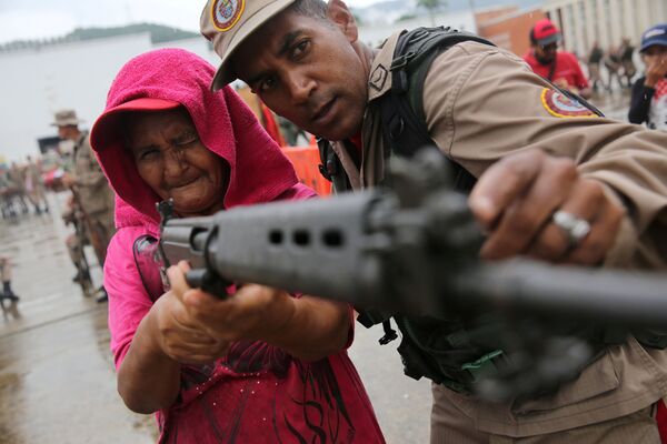 أحد أفراد قوات الشرطة الوطنية يدرب امرأة على حمل البندقية خلال تدريبات عسكرية في كاراكاس، فنزويلا 26 أغسطس/ آب 2017 - سبوتنيك عربي