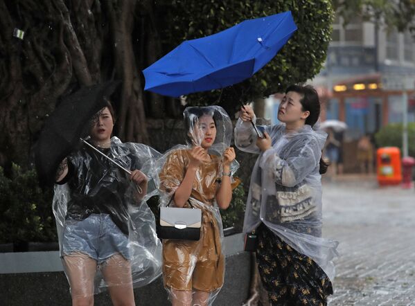 فتيات يحملن الشمسيات خلال إعصار في هونغ كونغ، 27 أغسطس/ آب 2017 - سبوتنيك عربي