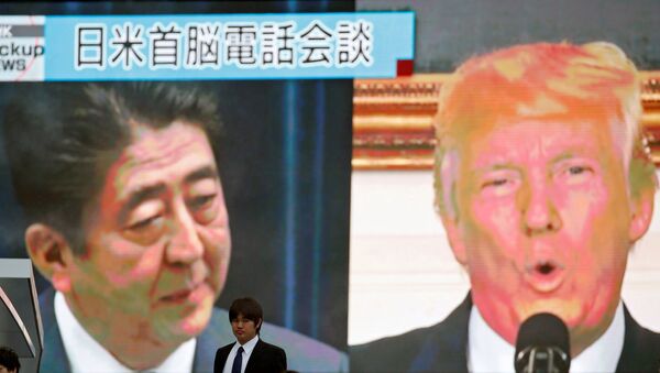 رجل يمشي قرب شاشة رصد تظهر رئيس الوزراء الياباني شينزو آبي والرئيس الأمريكي دونالد ترامب في تقرير إخباري عن اتصال هاتفي حول تهديد كوريا الشمالية، في طوكيو - سبوتنيك عربي