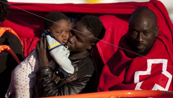 A migrants wrapped in a red cross blanket holds a child on arrival into the southern Spanish port of Malaga on January 27, 2016 after an inflatable boat carrying 55 Africans, seven of them women and six chidren, was rescued by the Spanish coast guard off the Spanish coast (File) - سبوتنيك عربي