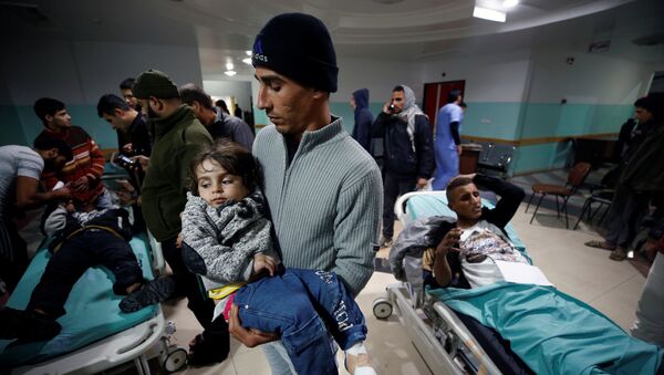 فلسطيني يحمل ابنته الجريحة وهي تنتظر تلقي العلاج بعد غارات جوية إسرائيلية قريبة من مستشفى في شمال قطاع غزة - سبوتنيك عربي