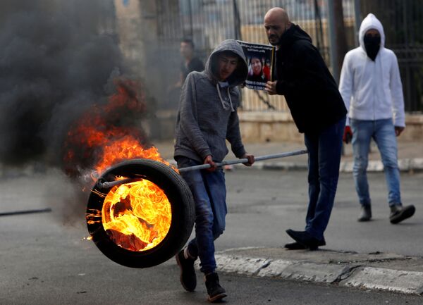 فلسطيني يحمل إطارا مشتعلا خلال المواجهات مع الشرطة الإسرائيلية في بيت لحم، الضفة الغربية، فلسطين 27 ديسمبر/ كانون الأول 2017 - سبوتنيك عربي