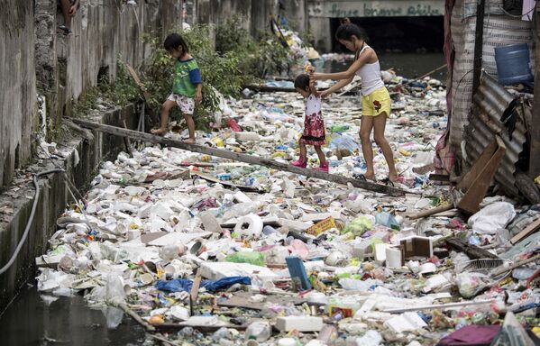 محليون يسيرون على لوح خشبي لعبور الممر المائي والقمامة في مانيلا 17 يناير/ كانون الثاني 2018 - سبوتنيك عربي
