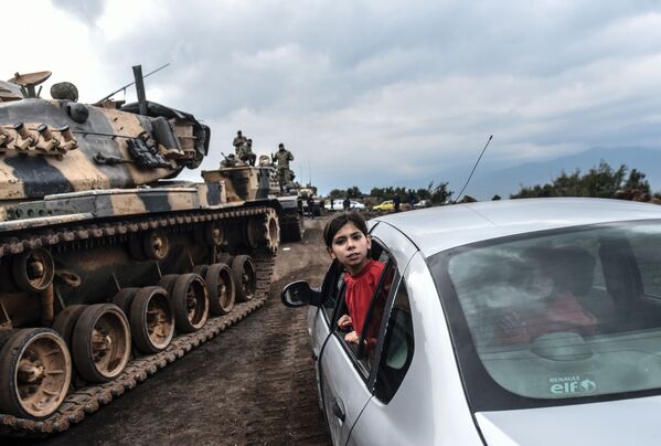 طفلة تركية تنظر عبر نافذة سيارة على خلفية تجمع لدبابات الجيش التركي على الحدود السورية التركية في هاتاي، 21 يناير/ كانون الثاني 2018 - سبوتنيك عربي