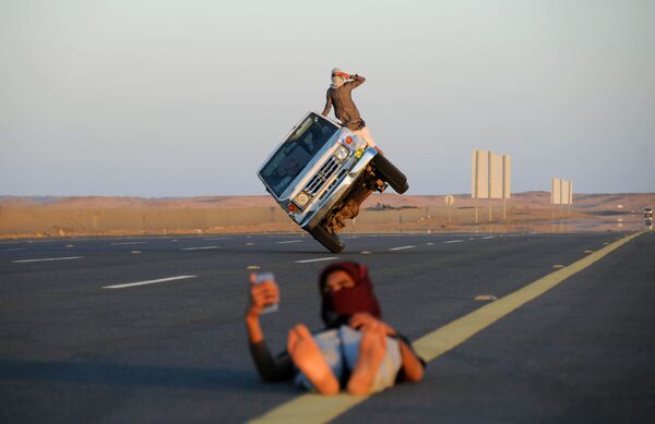 شاب يلتقط صورة سيلفي على خلفية شابين سعوديين يقودان سيارة على عجلتين فقط في تبوك، السعودية 11 مارس/ آذار 2018 - سبوتنيك عربي