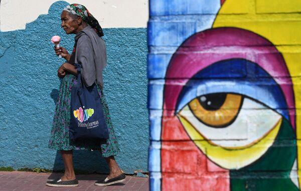 امرأة تسير حاملة مثلجات على خلفية جدارية في شارع فال دي أنجلوس، شمال تيغوسيغالبا في هندوراس 8 أبريل/ نيسان 2018 - سبوتنيك عربي