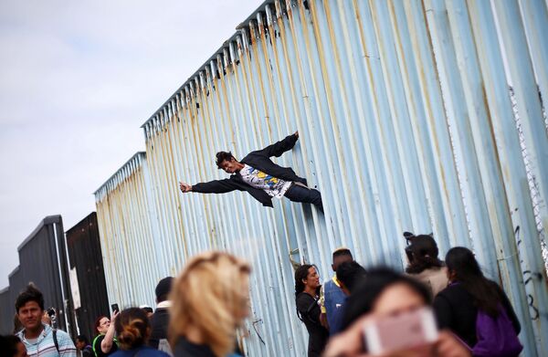 رجل يتسلق السياج الحدودي بين المكسيك والولايات المتحدة كجزء من المظاهرة، حيث يجتمع أعضاء من قافلة المهاجرين من أمريكا الوسطى قبل الاستعدادات لطلب اللجوء في الولايات المتحدة ، في تيخوانا، المكسيك 29 أبريل/ نيسان 2018 - سبوتنيك عربي