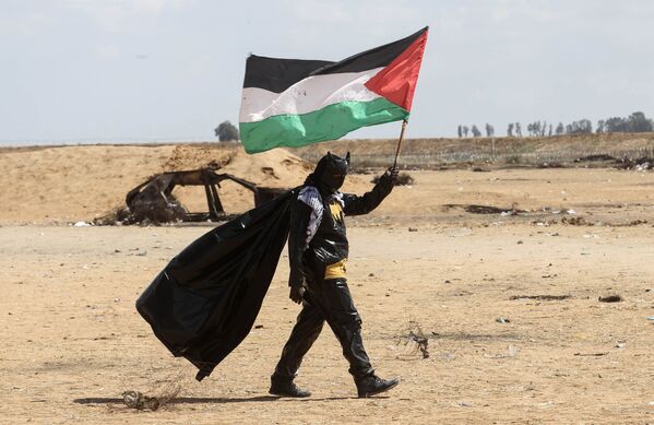 شاب فلسطيني يحمل العلم الفلسطيني، مرتديا زي ارجل الوطواط، خلال فعاليات مسيرات العودة في شرق خانيونس، على الحدود بين قطاع غزة وإسرائيل، 9 مايو/ أيار 2018 - سبوتنيك عربي