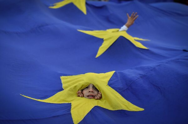 صبي يظهر من خلال ثقب في علم الاتحاد الأوروبي أثناء مسيرة في بوخارست، رومانيا، 12 مايو/ أيار 2018 - سبوتنيك عربي
