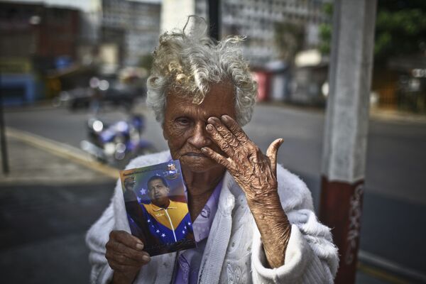 امرأة مسنة تحمل صورة الرئيس الفنزويلي الراحل هوغو تشافيز في كاراكاس - سبوتنيك عربي