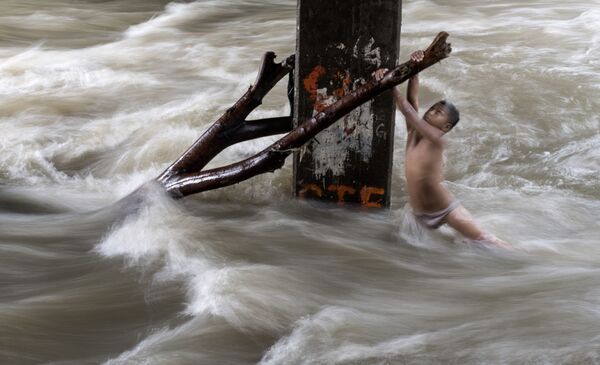 صبي يمسك بغصن شجرة خشية الانجرار في نهر فاض بسبب الأمطار الغزيرة في مانيلا، الفلبين 11 يونيو/ حزيران 2018 - سبوتنيك عربي