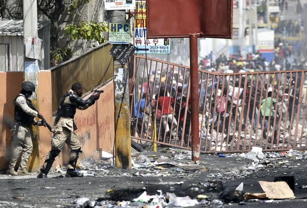 أحد أفراد الشرطة الهايتيّة يوجه مسدسه نحو الناس لتفادي النهب في المحلات التجارية في ديلماس، وهي بلدية قرب بورت-أو-برنس، خلال احتجاجات ضد ارتفاع أسعار الوقود، في 8 يوليو/ تموز 2018 - سبوتنيك عربي