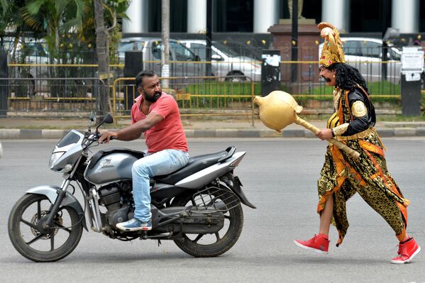 فنان يرتدي زي ياماراج (يمين الصورة)، وهو إله الموت الهندوسي، يركض خلف سائق يركب دراجة نارية بدون خوذة. وذلك في إطار حملة أسبوع السلامة على الطرق، التي نظمتها شرطة المرور في بنغالور في 10 يوليو/ تموز 2018. - سبوتنيك عربي