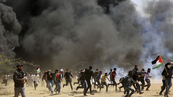 Palestinian protesters run to cover from teargas fired by Israeli soldiers during clashes with Israeli troops along Gaza's border with Israel, east of Khan Younis, Gaza Strip, Friday, April 6, 2018 - سبوتنيك عربي