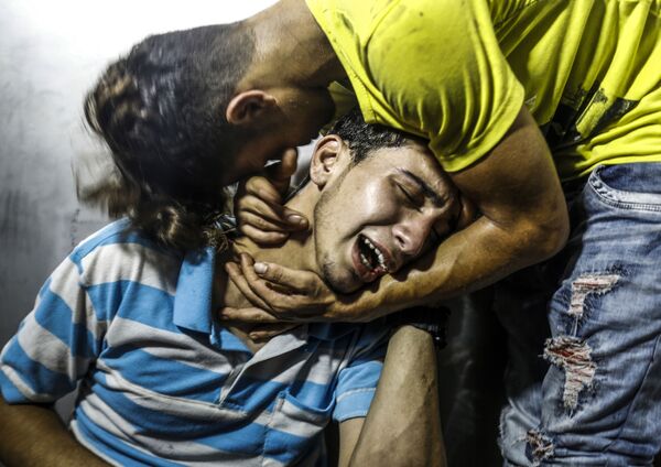 شباب فلسطينيون يبكون شابين قتلا في غارة جوية إسرائيلية في مدينة غزة، قطاع غزة، فلسطين 14 يوليو/ تموز 2018 - سبوتنيك عربي