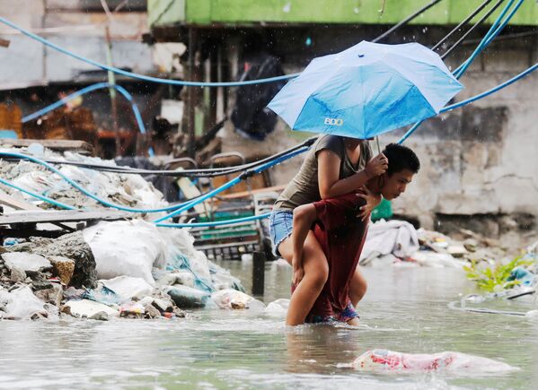 رجل يحمل امرأة على ظهره لعبور شارع مغمور بالمياه بعد  هطول أمطار موسمية وعاصفة مدارية سون-تينه في مدينة كويزون، مترو مانيلا، في الفلبين 17 يوليو/ تموز 2018 - سبوتنيك عربي